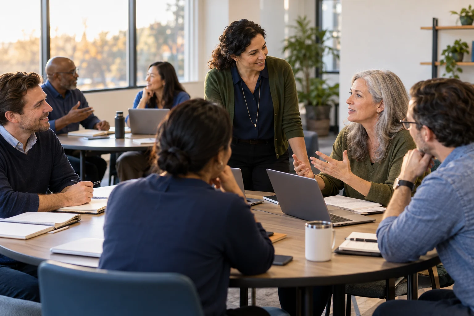 Adult professionals participating in a continuing education seminar with a trainer in a warmly lit classroom.